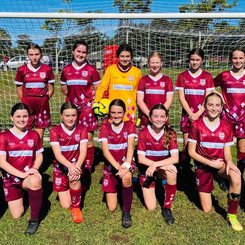 Group of Iona Sports Club soccer players in maroon C2C Sport uniforms with a goalkeeper in a yellow uniform, posing in front of a goal.
